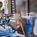 Confident man washing car mats on self-service car-washing station.