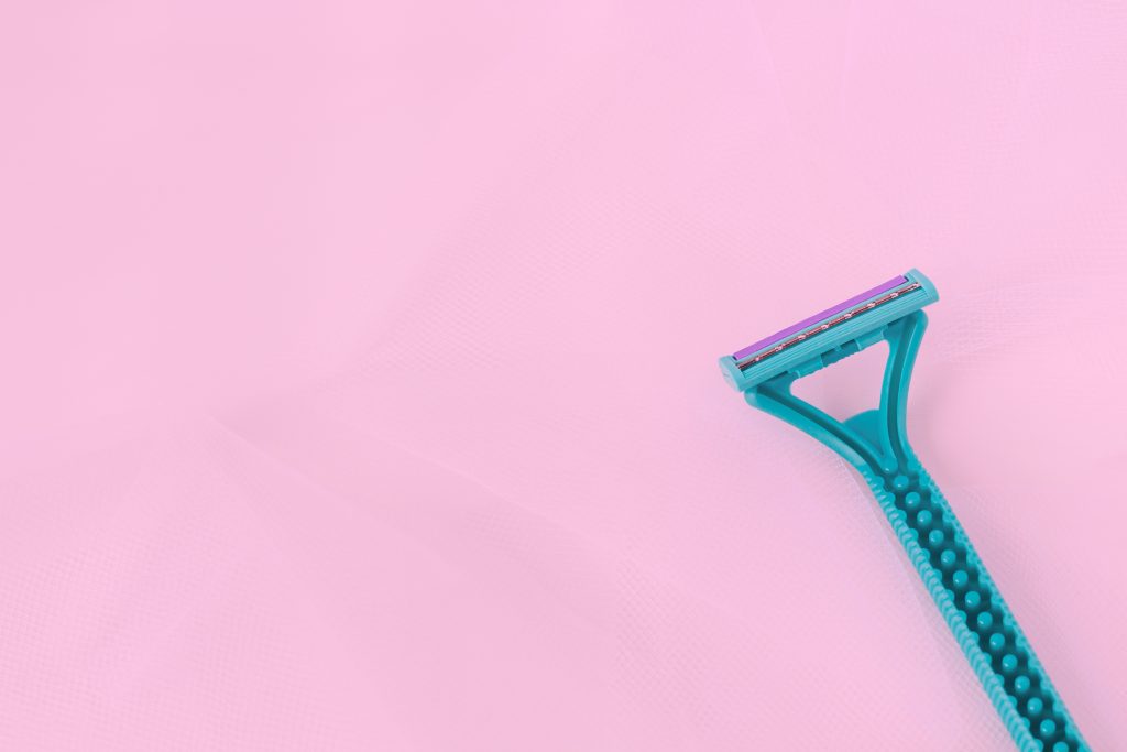 Female blue disposable razor above pink neaon background. Female shaving concept. Removing body hair