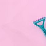 Female blue disposable razor above pink neaon background. Female shaving concept. Removing body hair