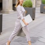 Self assured female manager with laptop crossing street near building